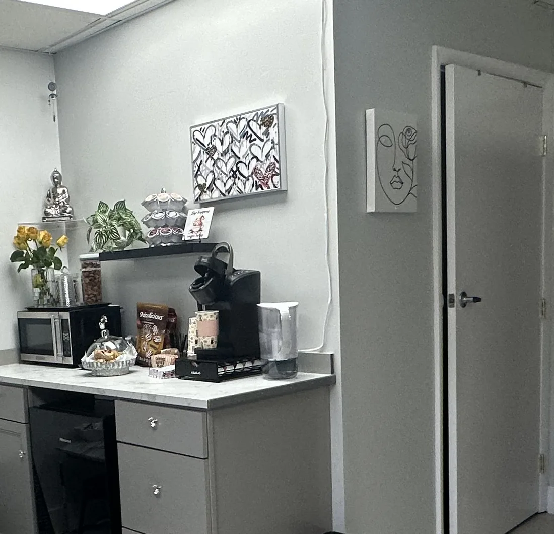 The studio's welcome corner, with a pod coffee maker, a water pitcher, snacks and a vase of yellow roses